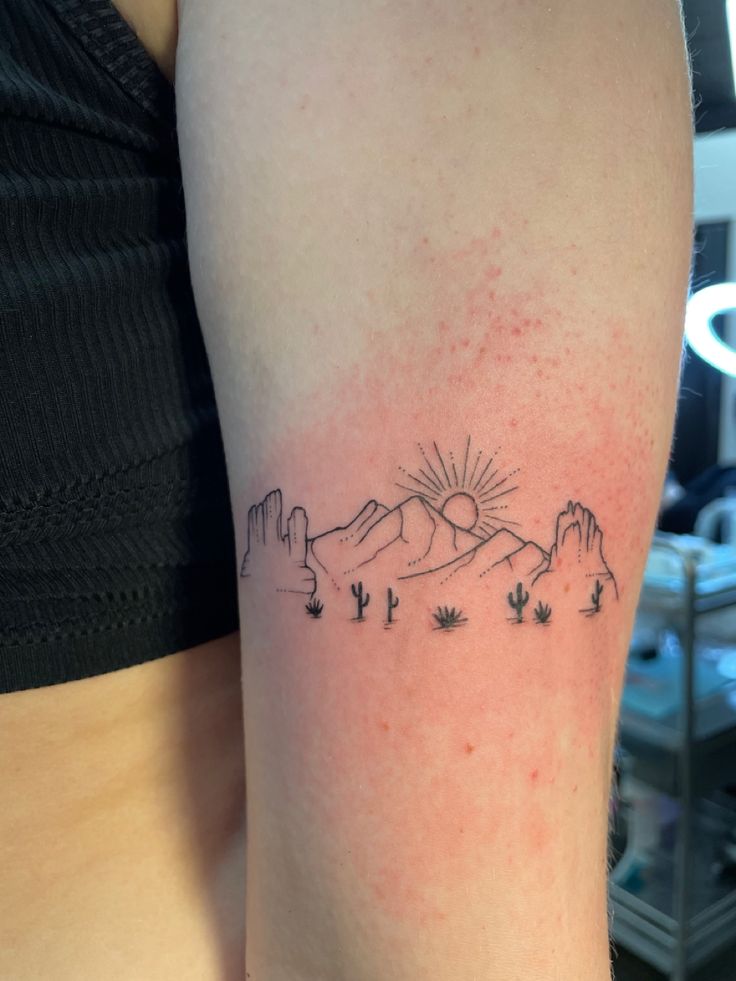 a woman's arm with a tattoo on it that has mountains and trees in the background