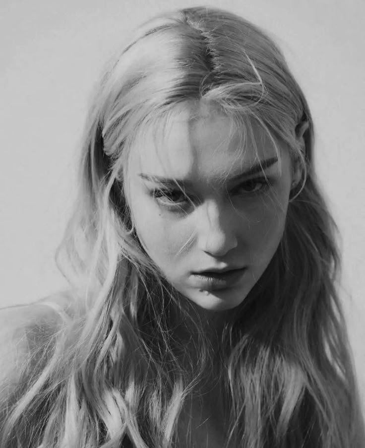 black and white photograph of a woman with long blonde hair looking at the camera while wearing a dress