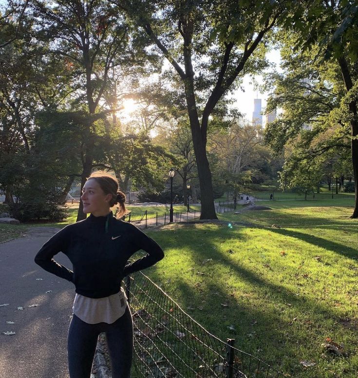 a woman is standing in the park with her hands on her hips and looking off into the distance