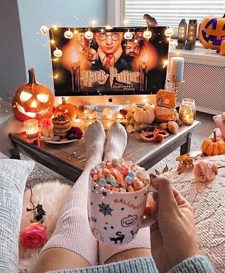 a person holding a cup with candy in front of a halloween scene on the tv