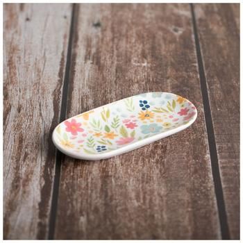 a white and yellow flowered plate sitting on top of a wooden table next to a knife