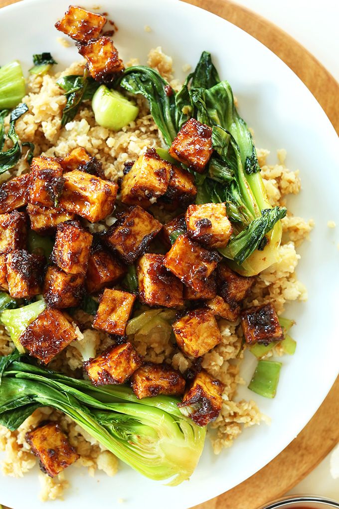 a white plate topped with tofu and broccoli on top of brown rice