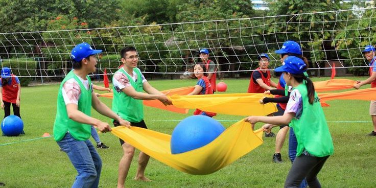 several people in green shirts and blue hats are playing volleyball on the grass with balls