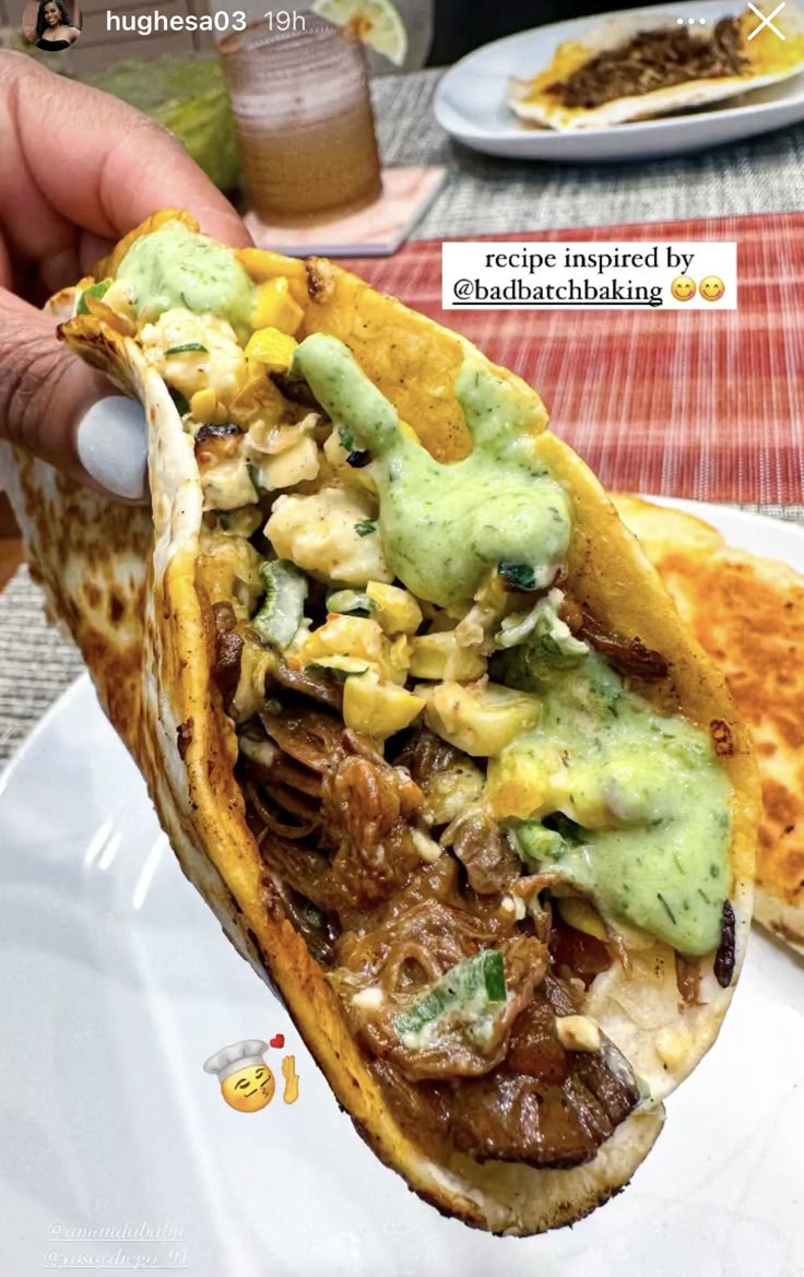 a person holding up a taco filled with meat and guacamole sauce