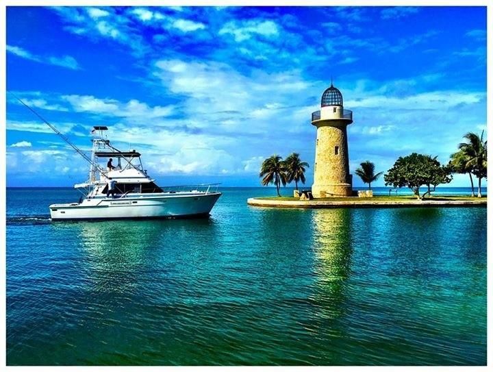 two boats are in the water near a light house and palm trees on an island