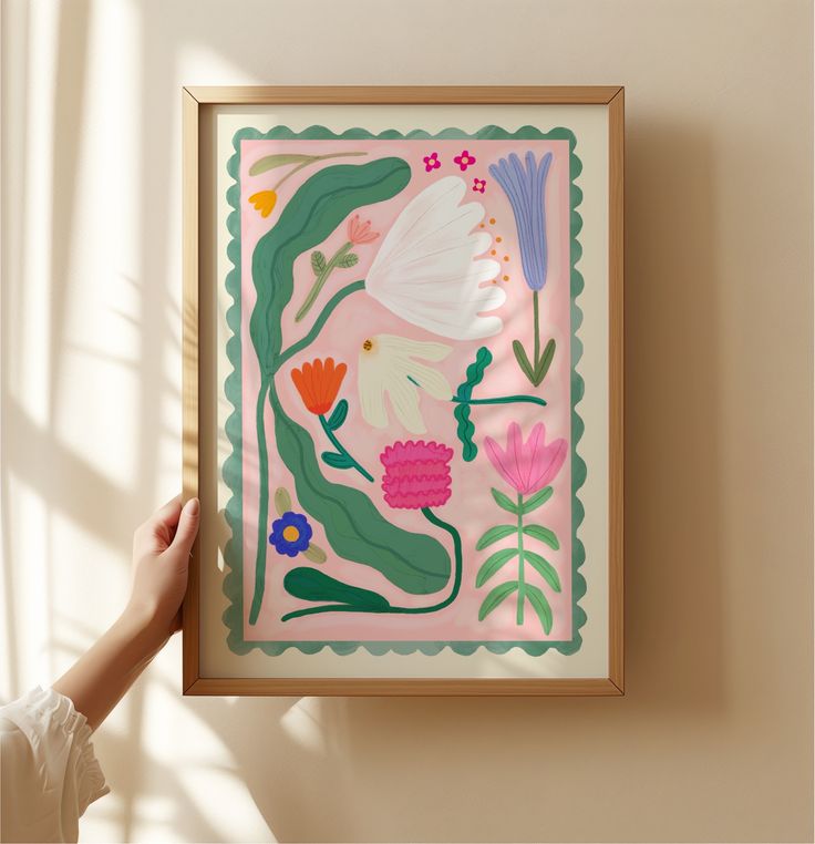 a person holding up a painting with flowers and plants on it in front of a window