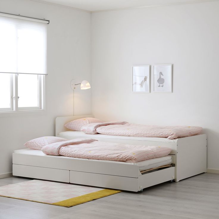 two white beds with pink sheets and pillows in a room next to a yellow rug