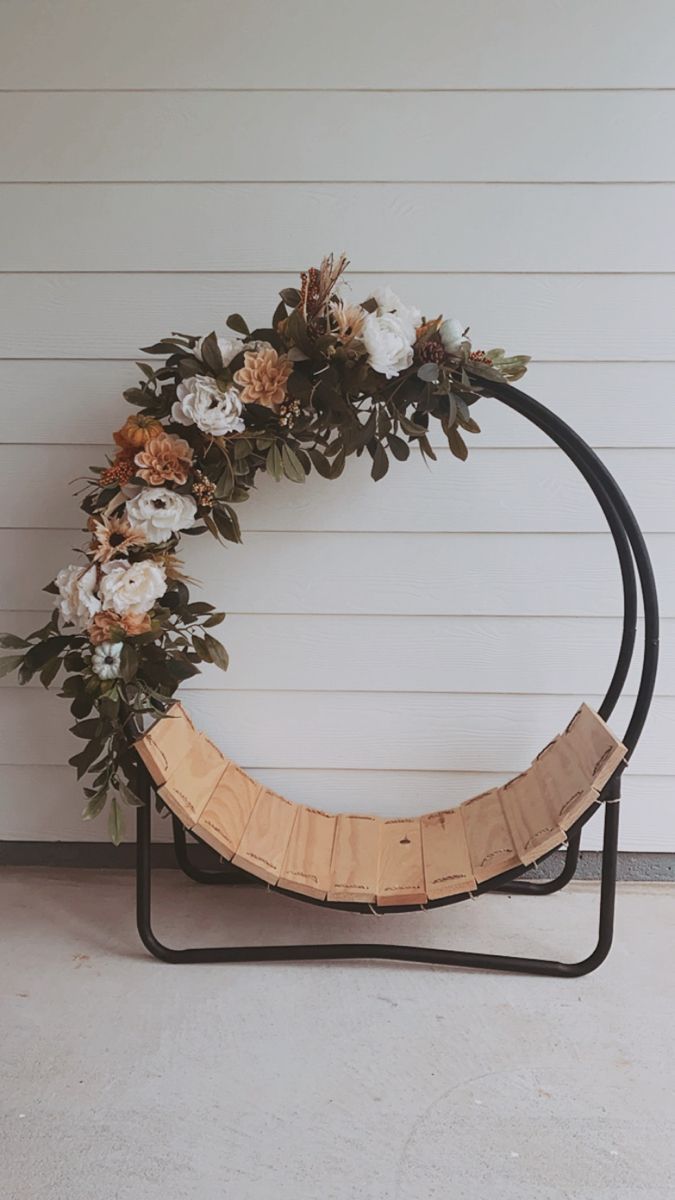 a wreath made out of wood and flowers on a black metal stand against a white wall