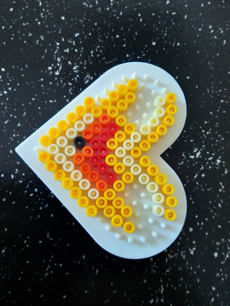 a plastic brooch with yellow and red beads on it's side, sitting on a black surface