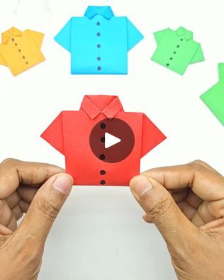 two hands holding up an origami piece with different colored paper pieces surrounding it