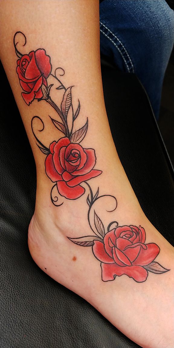 a woman's foot with red roses on it and leaves coming out of the top