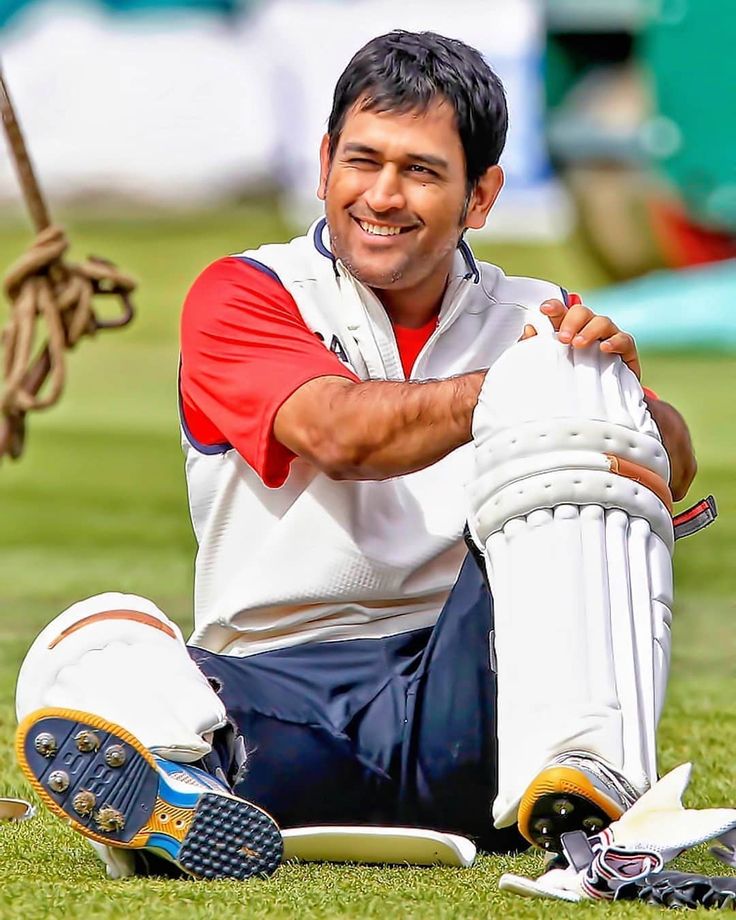 a man sitting on the ground holding a cricket bat and ball in his hands while smiling at the camera