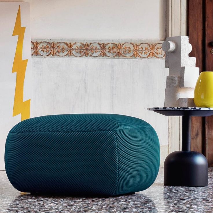 a blue ottoman sitting on top of a table next to a yellow vase and lamp