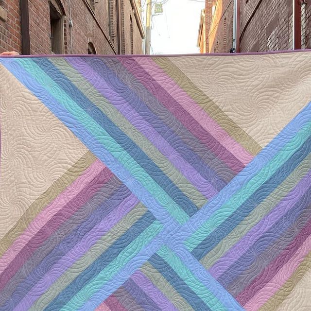 a large quilt hanging from the side of a building on a clothes line in an alleyway