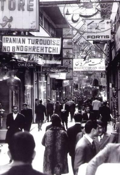 black and white photograph of people walking down the street in an old fashion town with stores on both sides