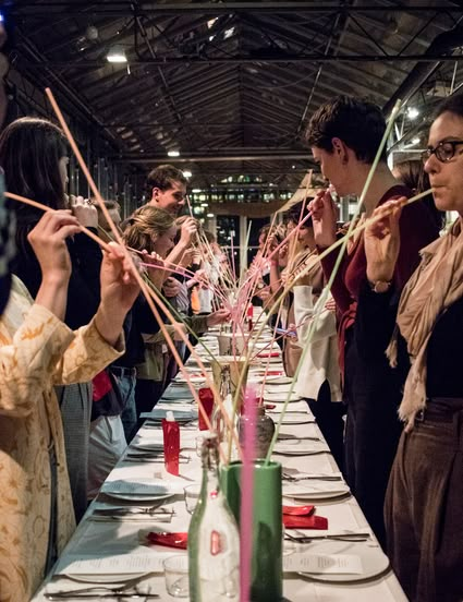 a group of people standing around a long table with plates and glasses on it,