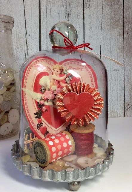 a glass cloche with buttons and thread in it next to a vase filled with hearts