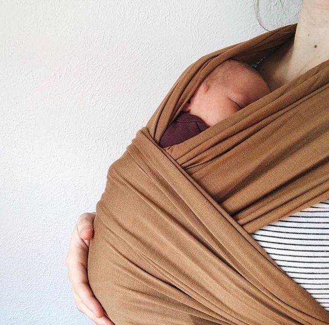 a woman holding a baby wrapped in a brown wrap on her chest and wearing a striped shirt