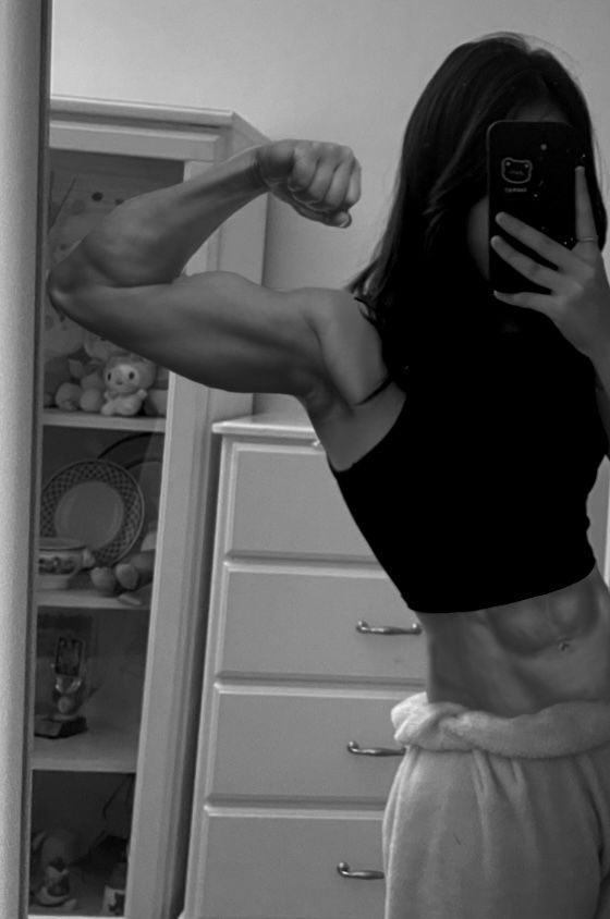 a woman taking a selfie in the mirror with her cell phone and showing off her muscles