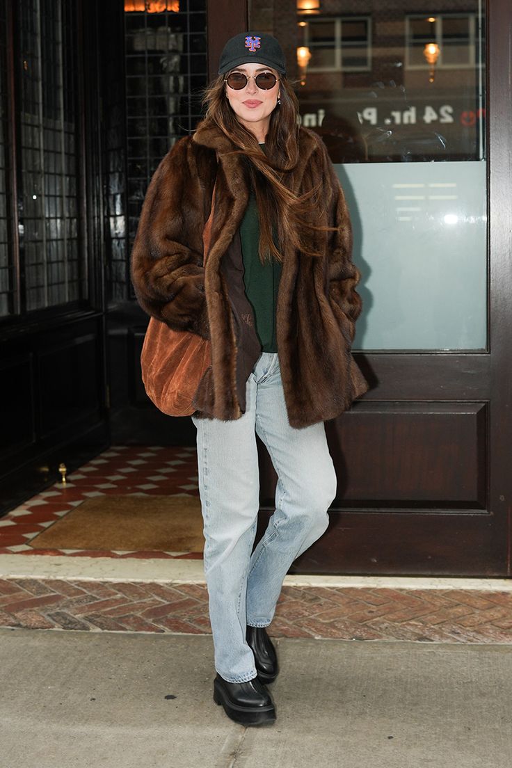 a woman standing in front of a building wearing a fur coat and hat with sunglasses on