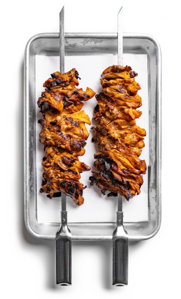 chicken skewers on a tray with tongs in the shape of two wings