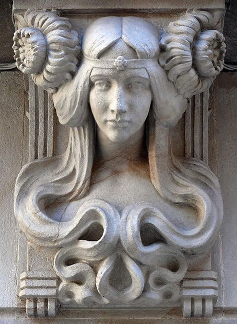 a close up of a statue on the side of a building with flowers in her hair