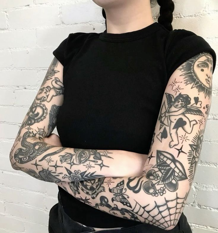 a woman with her arms crossed and tattoos on her body is standing in front of a white brick wall