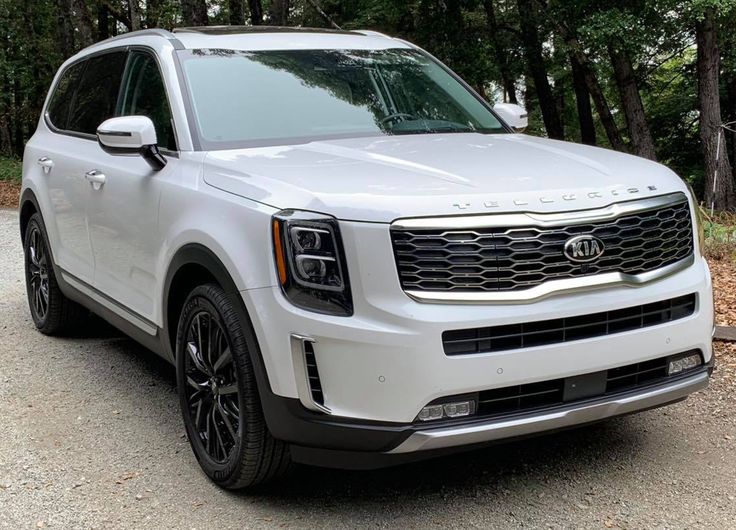 the front end of a white suv parked on a road near some trees and bushes