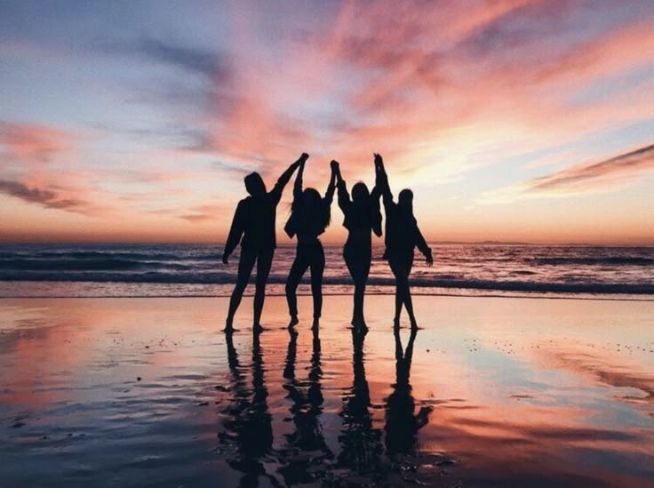 three people standing on the beach with their arms in the air at sunset or dawn