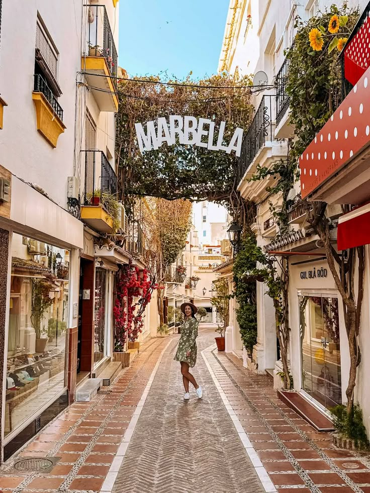 a woman is walking down the street under an arch that says marbella on it