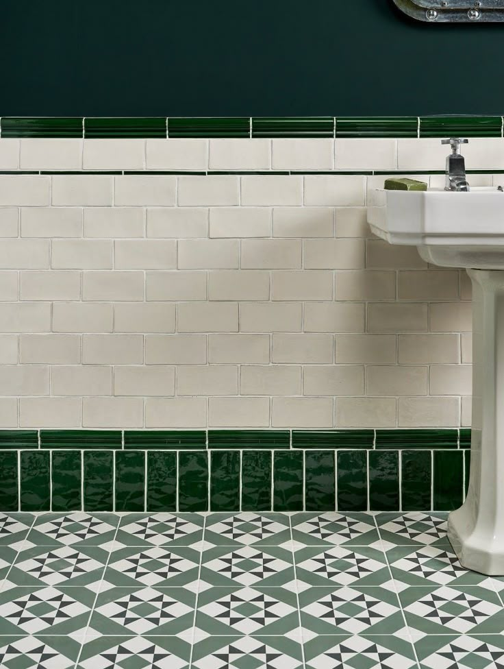 a bathroom with green and white tiles on the floor, sink and mirror above it