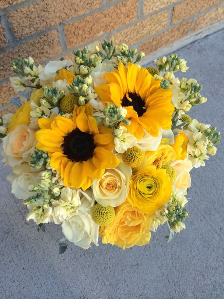 a bridal bouquet with sunflowers and other flowers in it on the sidewalk