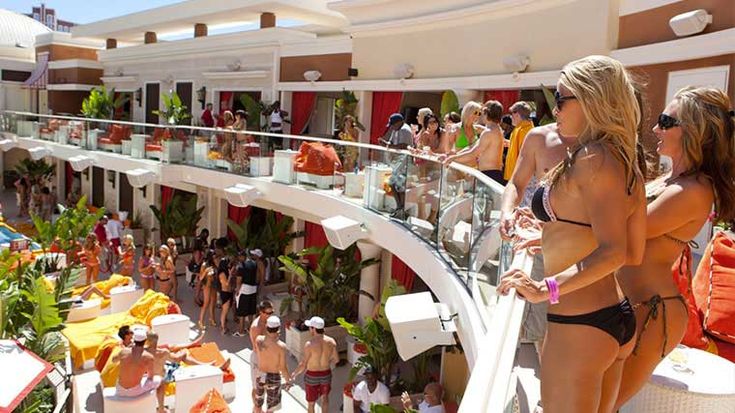 two beautiful women in bikinis standing on a balcony next to a crowd of people