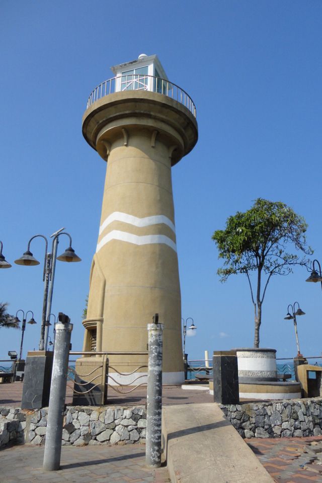 a tall light house sitting on top of a stone wall next to the ocean and trees