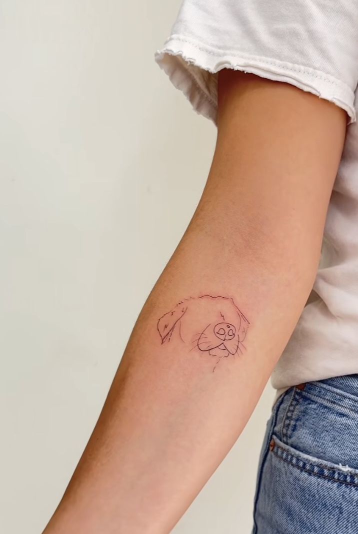 a woman's arm with a small dog tattoo on the left side of her arm