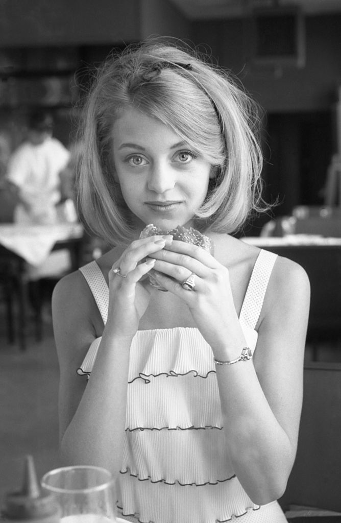 a black and white photo of a woman at a table eating a doughnut in a restaurant