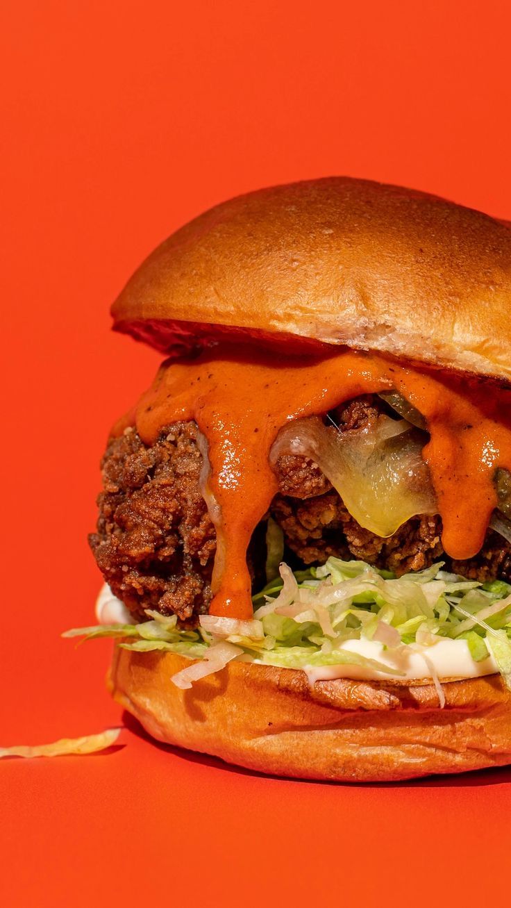 a hamburger with meat, cheese and lettuce on an orange background is shown