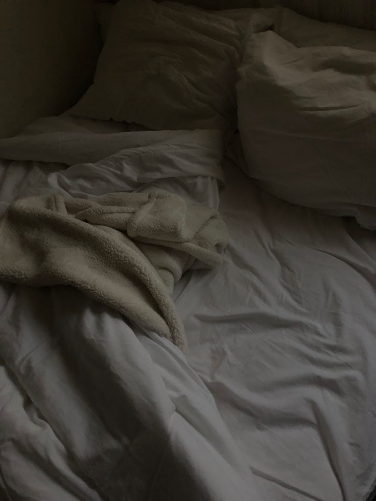 an unmade bed with white sheets and blankets on top of it in a dark room