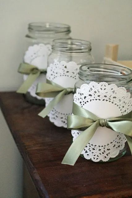 four mason jars with lace doily and green bows on them sitting on a table