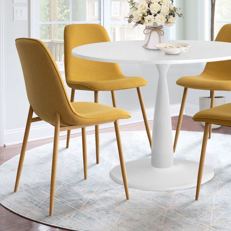 a white table with four yellow chairs around it and a vase filled with flowers on top