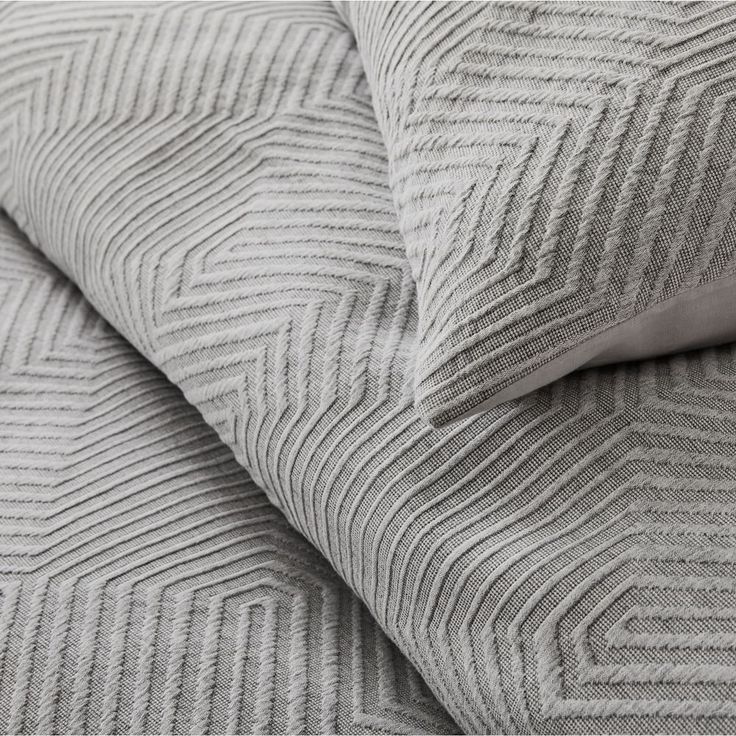 a close up view of the textured bedding and pillows on a white bed