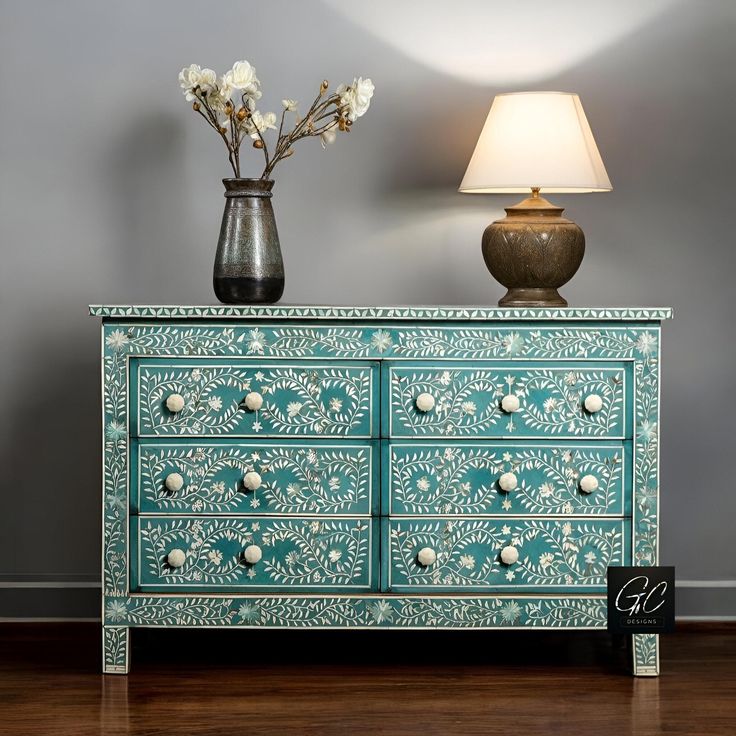 a green painted dresser with flowers and a lamp