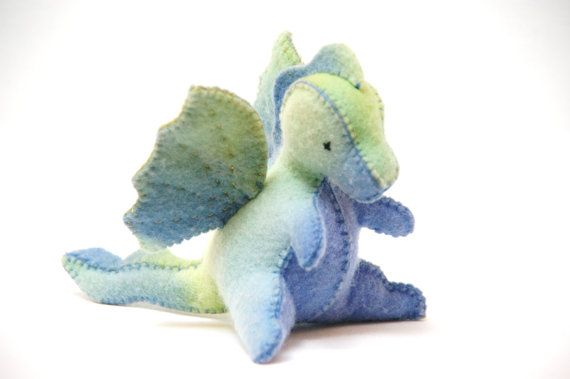 a blue and green stuffed dragon sitting on the ground with its wings spread out,