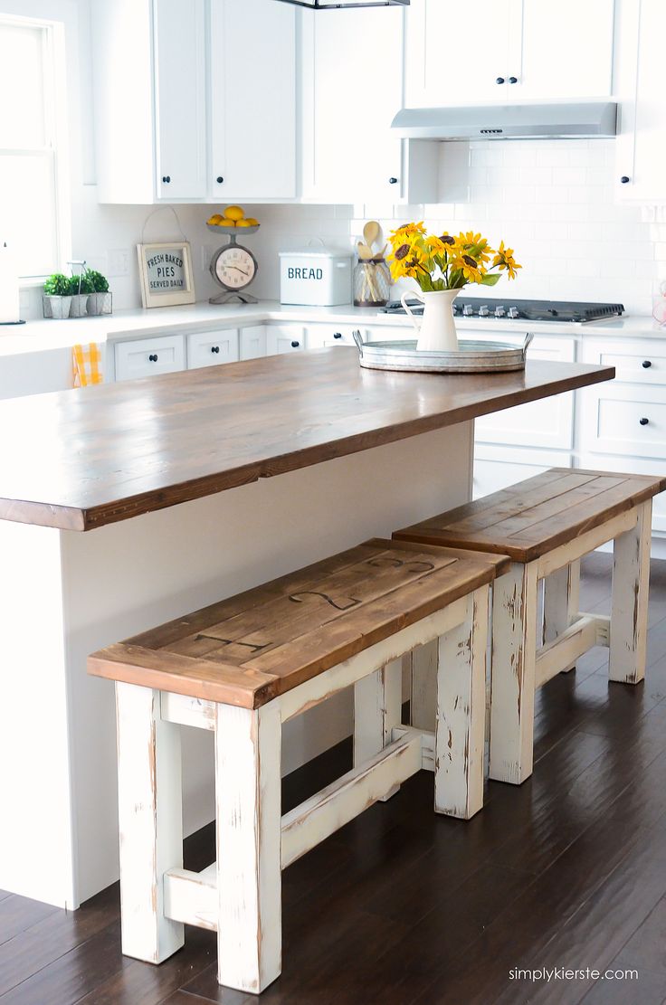 a kitchen island with two benches in front of it and sunflowers on the counter