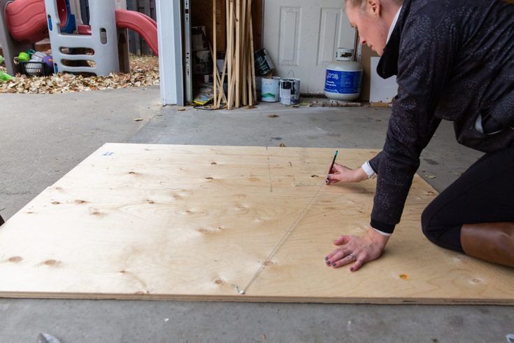 a man kneeling down on top of a piece of plywood with a pencil in his hand