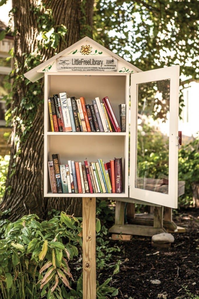 a book shelf with books on top of it in the middle of a yard next to a tree