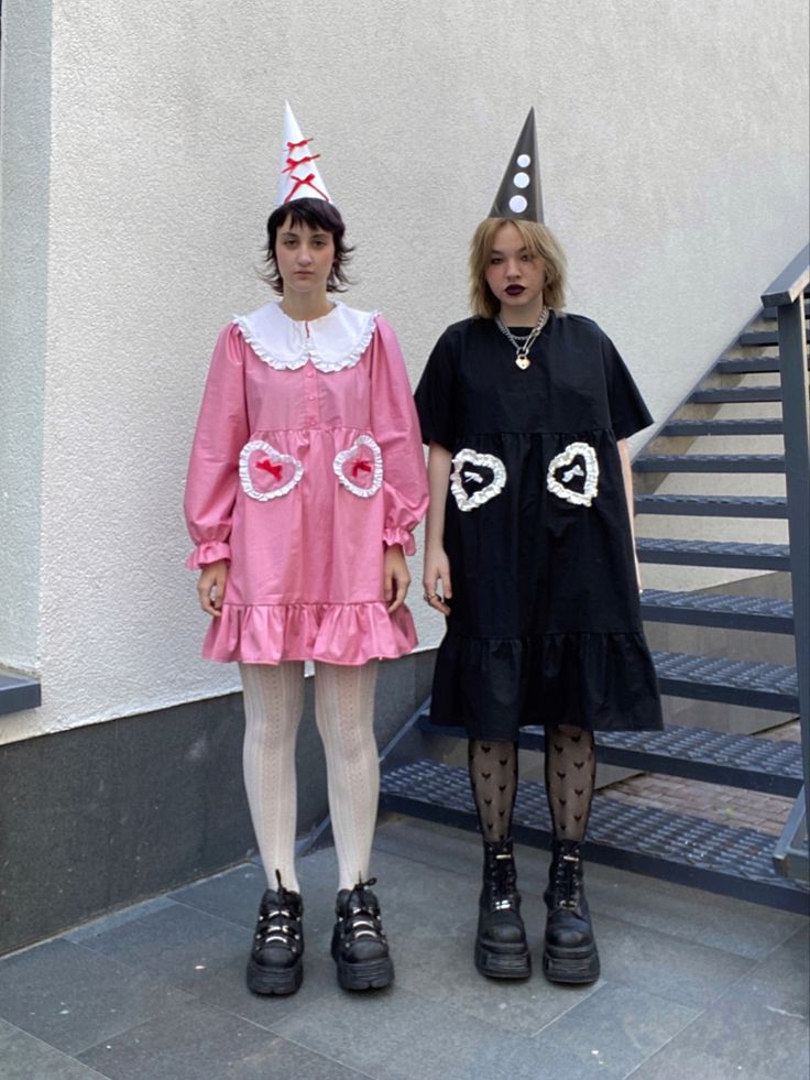 two women standing next to each other in front of a building wearing birthday hats and dresses