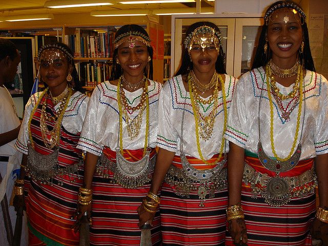 three women in ethnic garb standing next to each other with bookshelves behind them