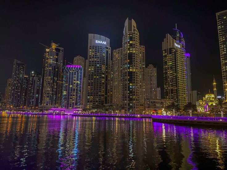 the city skyline is lit up at night with bright lights reflecting in the water and skyscrapers