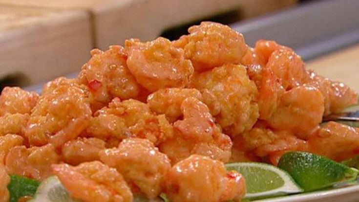 a white plate topped with fried shrimp and green peppers on top of a wooden table